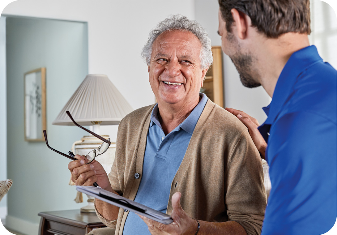 Female clinician reviews paperwork with elderly man at home, masked
